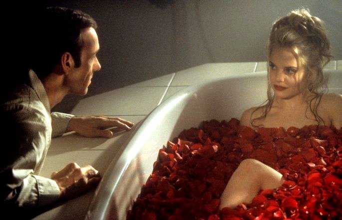 Ángela recostada en una bañera con pétalos rojos y Lester afuera.