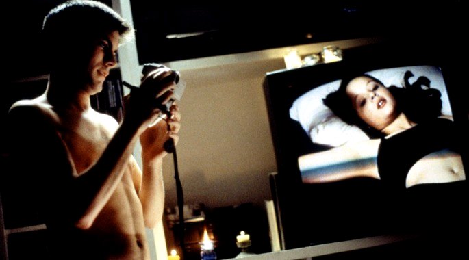 Jane tumbada en la cama y Ricky, de pie, filmándola.