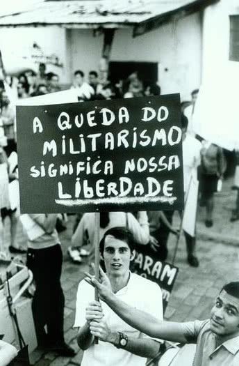 Fotografía de una protesta de 1968, un joven sostiene un cartel que pide el fin del militarismo.