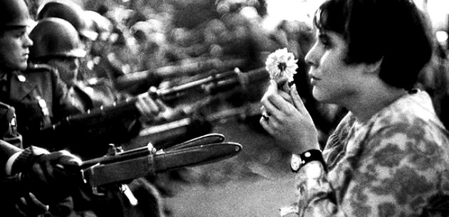 Retrato de una mujer de los años 60 sosteniendo una flor frente al ejército.