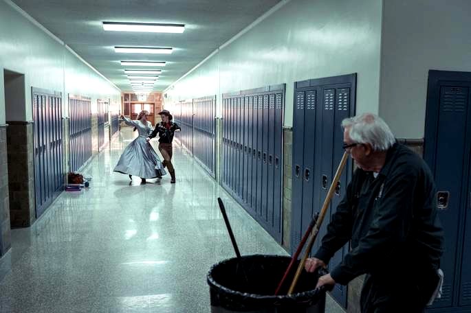 Un conserje viendo a una pareja bailando en el salón de la escuela