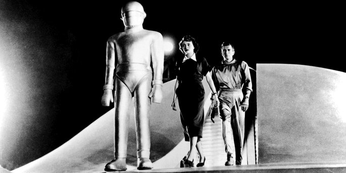 Un hombre, una mujer y alguien con traje de astronauta saliendo de una nave espacial.