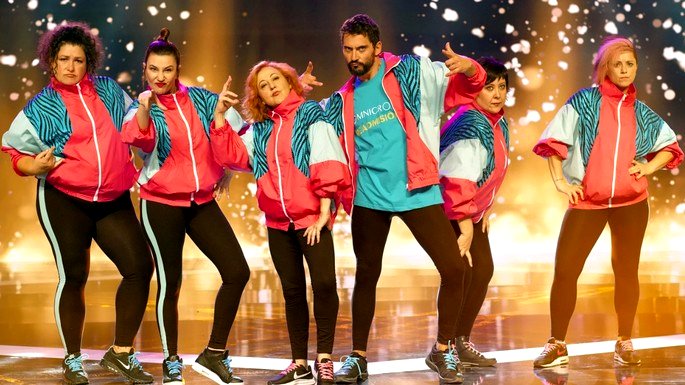 Cine Tribu Urbana baile. Un grupo de mujeres y hombres de pie en ropa de gimnasia en un escenario iluminado